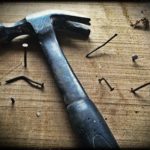 Hammer and bent nails are scattered on a wooden board, ready for installation on a hardwood floor.