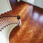 Curved wooden staircase with white balusters gracefully overlooks a polished herringbone-patterned hardwood floor, exceeding refinishing expectations.
