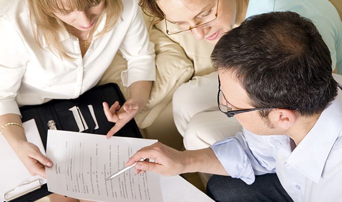 Three people reviewing documents together, with one person pointing at the papers on a table, attentively working through the Homeowner Checklist to ensure nothing is overlooked.