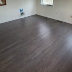Room with dark wood flooring, white walls, and two windows. There's a small patch of tools on the floor by the wall.