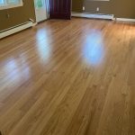 An empty room with light wood flooring, beige walls, white trim, and an open maroon door.
