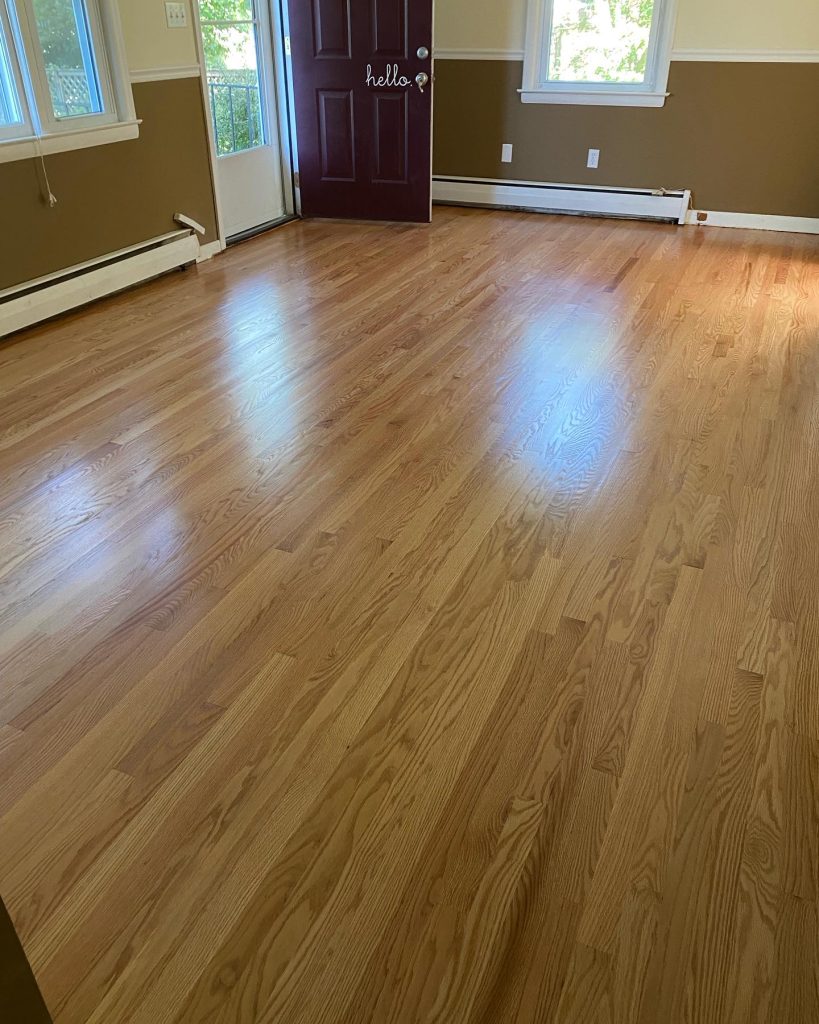 An empty room with light wood flooring, beige walls, white trim, and an open maroon door.