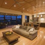Modern open-plan living room and kitchen with wood floors, large windows, and neutral-toned furniture.