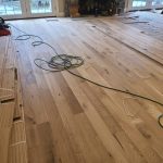 Wood flooring being installed in a room, with an air compressor and a green hose on the floor.
