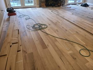 Wood flooring being installed in a room, with an air compressor and a green hose on the floor.