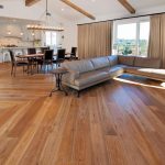Open living room with wood floors, a brown sectional sofa, dining table, and large windows with beige curtains.