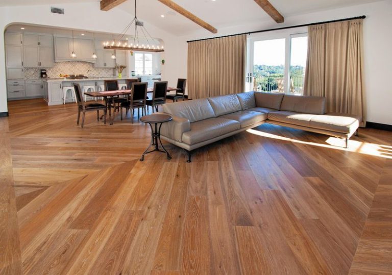 Open living room with wood floors, a brown sectional sofa, dining table, and large windows with beige curtains.