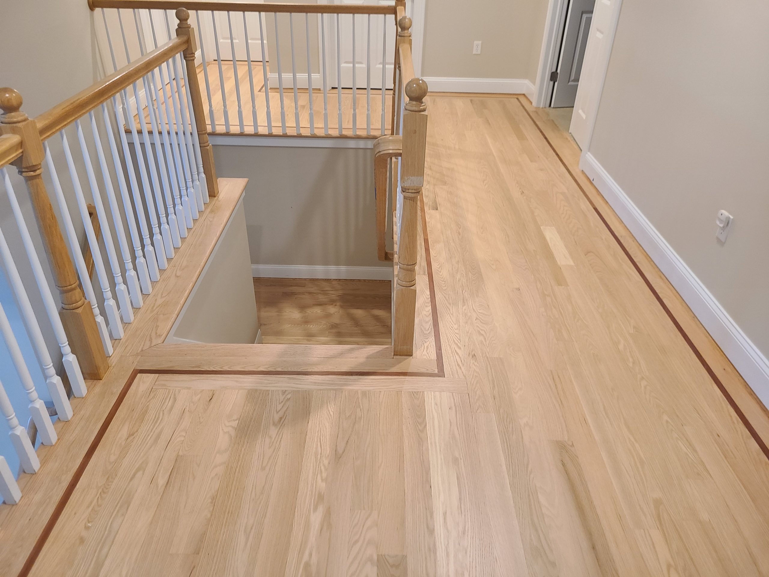 Upstairs hallway with light wood floors, white walls, and a staircase with wooden handrails and white spindles.