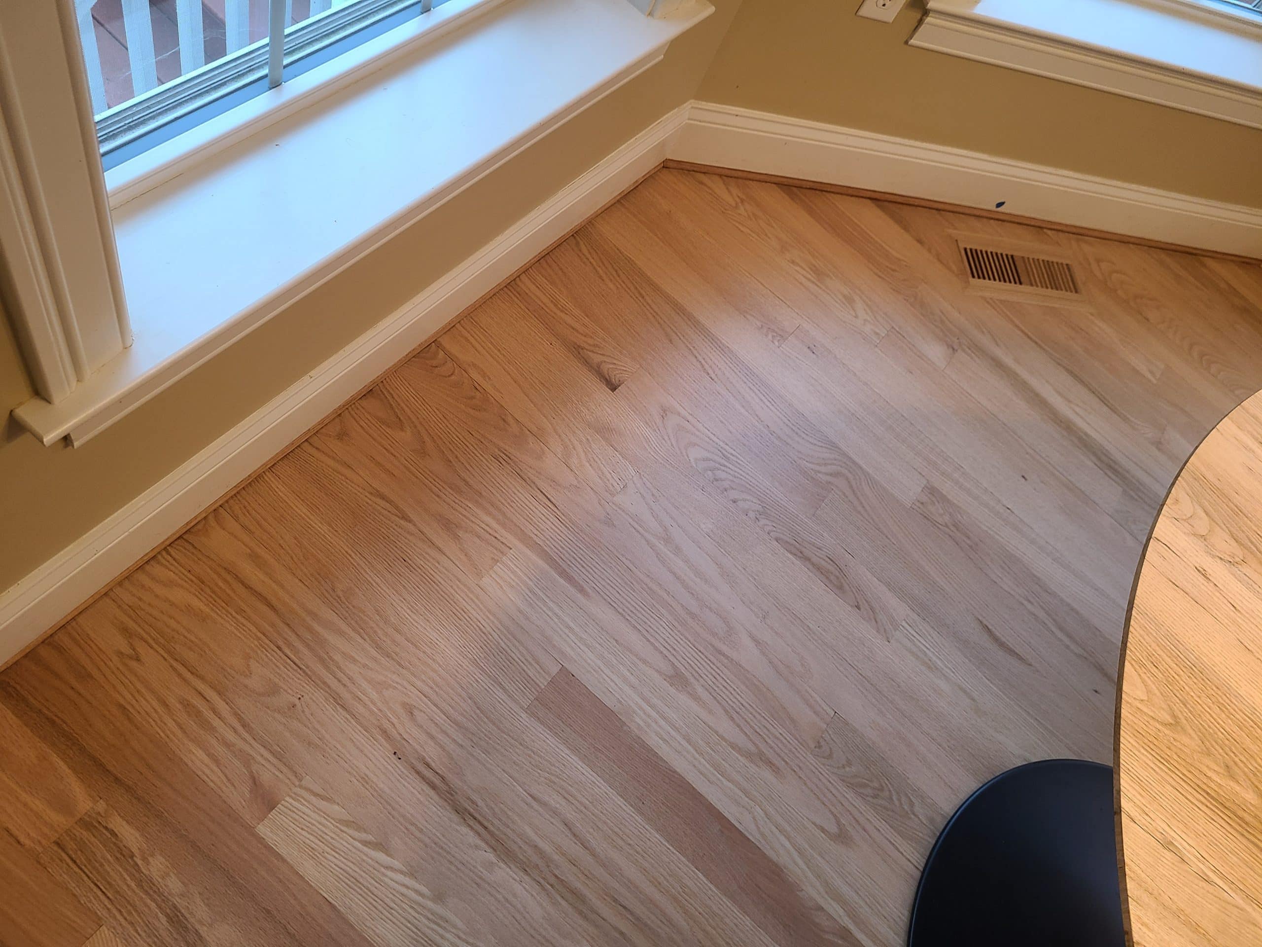 Corner of a sunlit room with light wood flooring, beige walls, and part of a round table visible.
