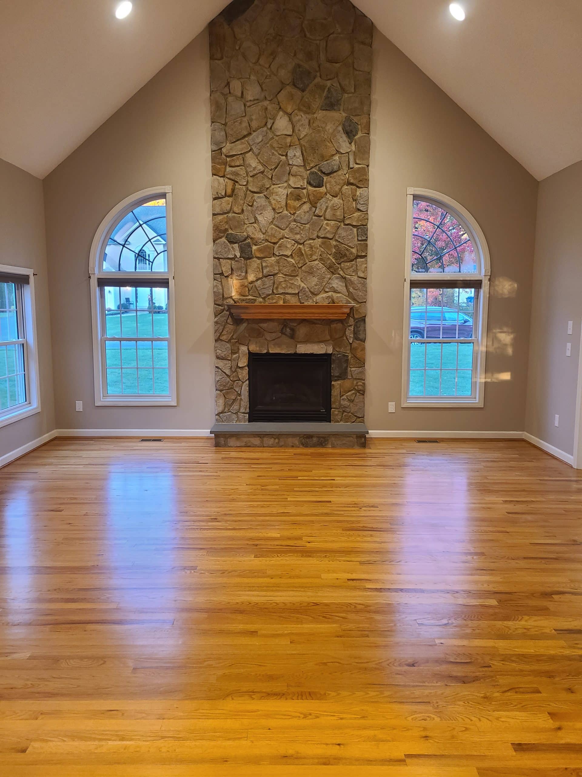 Spacious room with hardwood floors, stone fireplace, and two arched windows on either side.