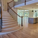 Curved wooden staircase in an open, modern home with large windows, light wood floors, and a kitchen island.