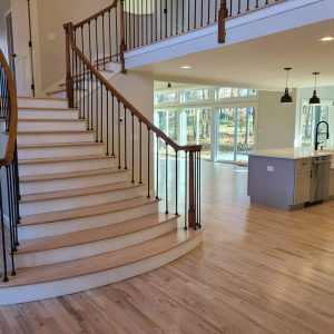Curved wooden staircase in an open, modern home with large windows, light wood floors, and a kitchen island.