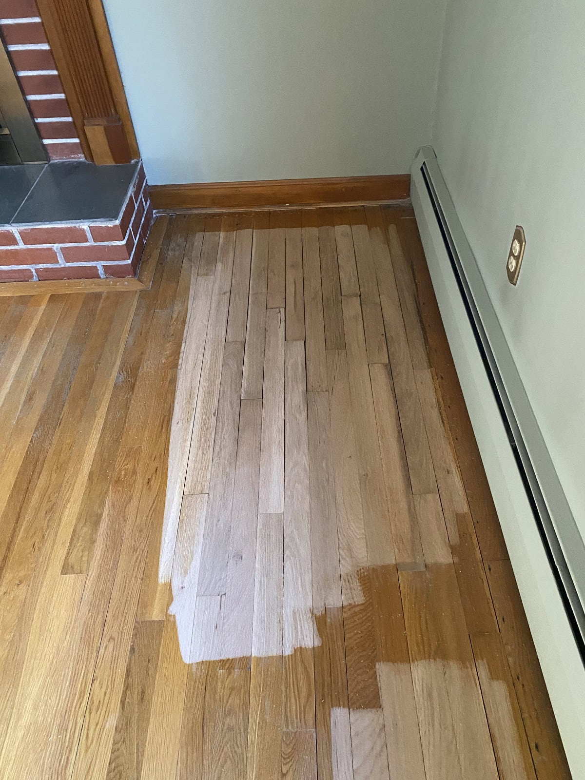 Hardwood floor refinishing in Wethersfield home showing sanded oak planks next to existing finish near brick fireplace