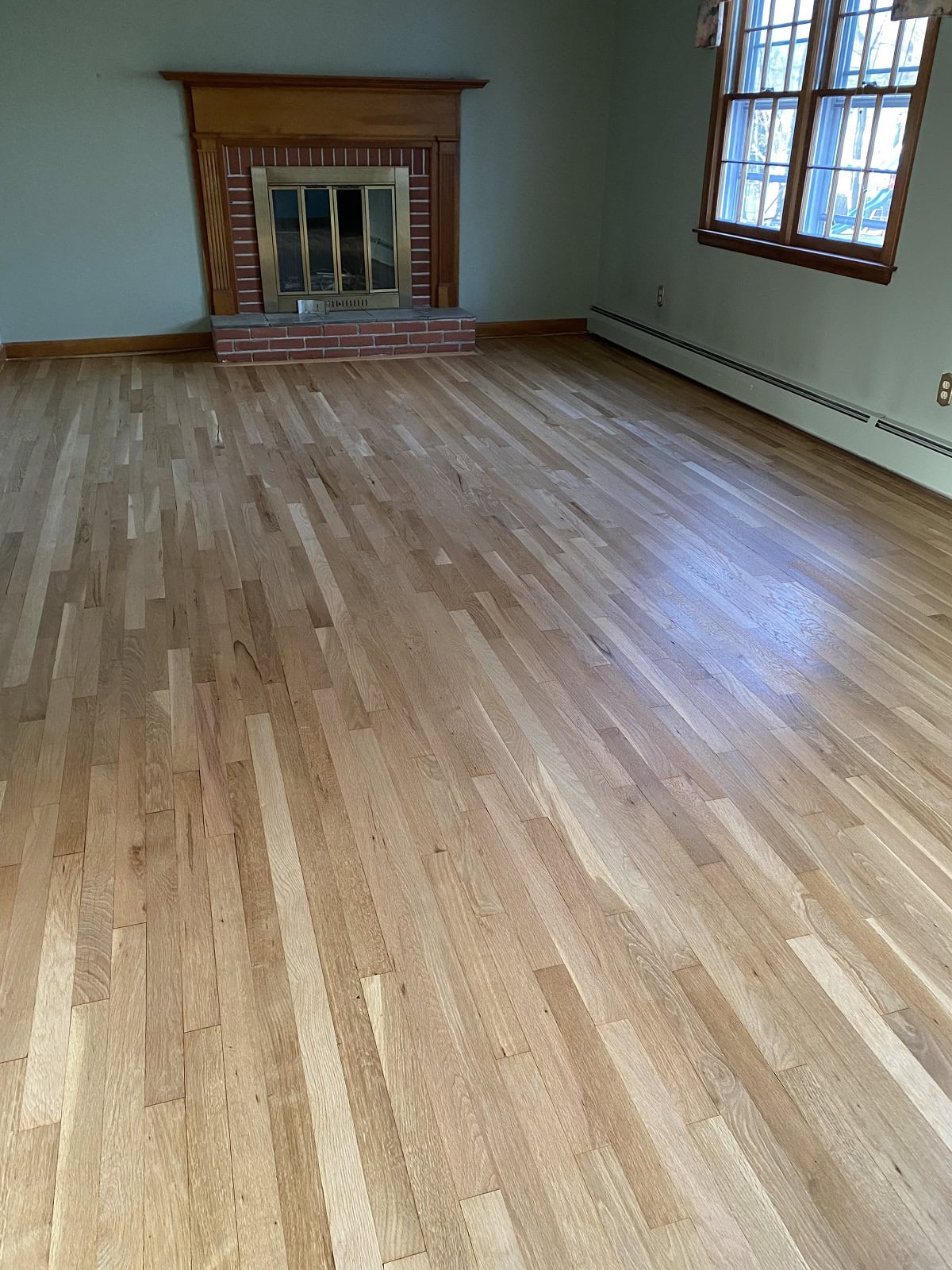 Oak hardwood flooring in Wethersfield living room with brick fireplace, natural wood finish, and seamless plank installation