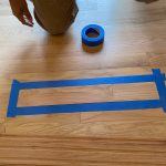Hardwood floor repair technician marking a single oak board with blue painter's tape in a Cromwell CT foyer.